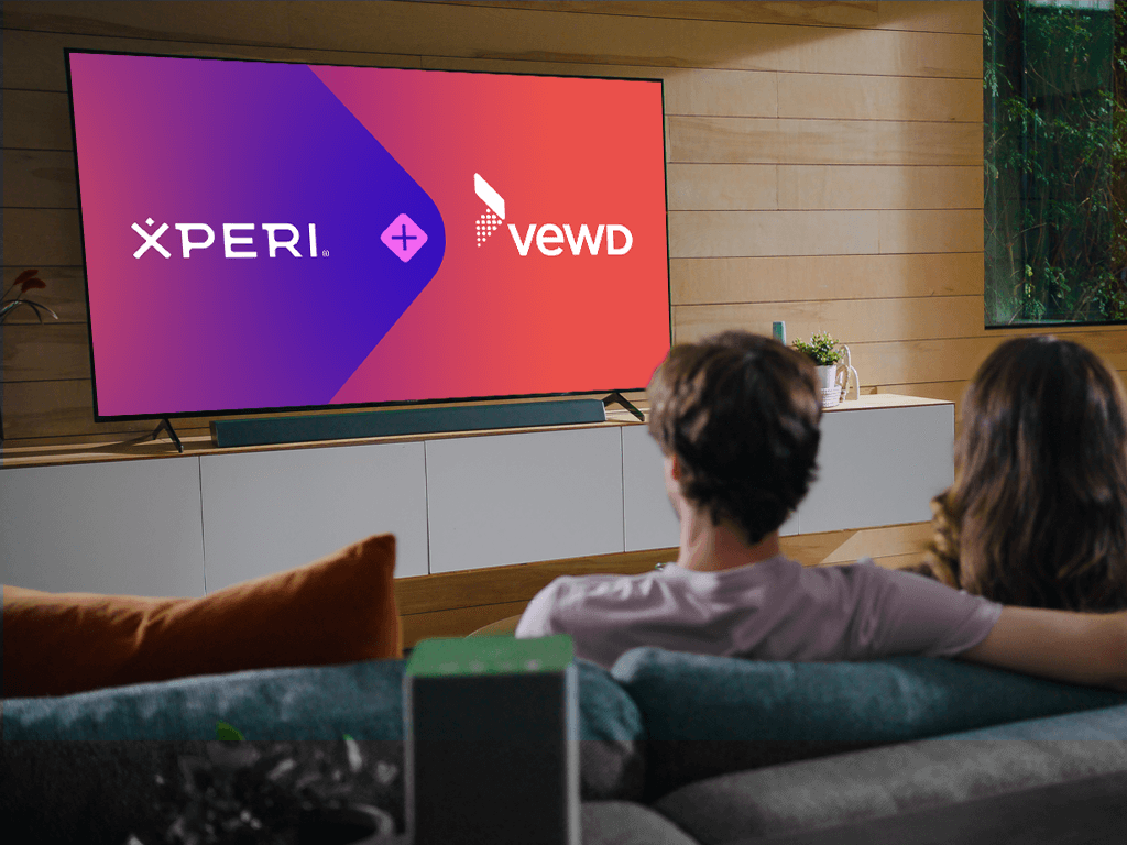 Two people looking at a tv with the xperi and vewd logos